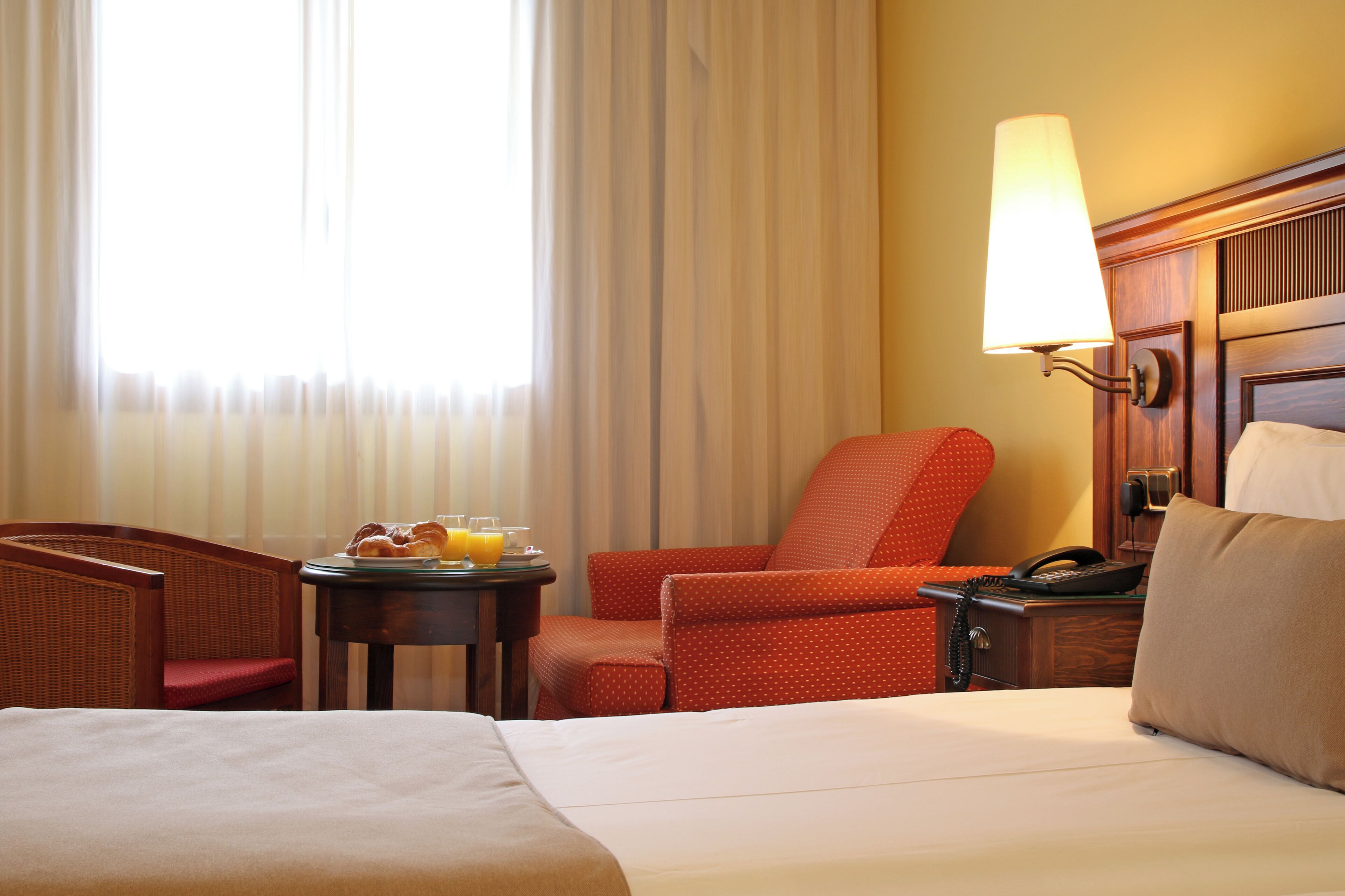 Habitación de hotel con cama, una silla, una mesita con desayuno, lámpara y teléfono.