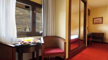 Een hotelkamer met een ontbijt gedekte eettafel, een rieten stoel, een spiegel en een klein bureau.
