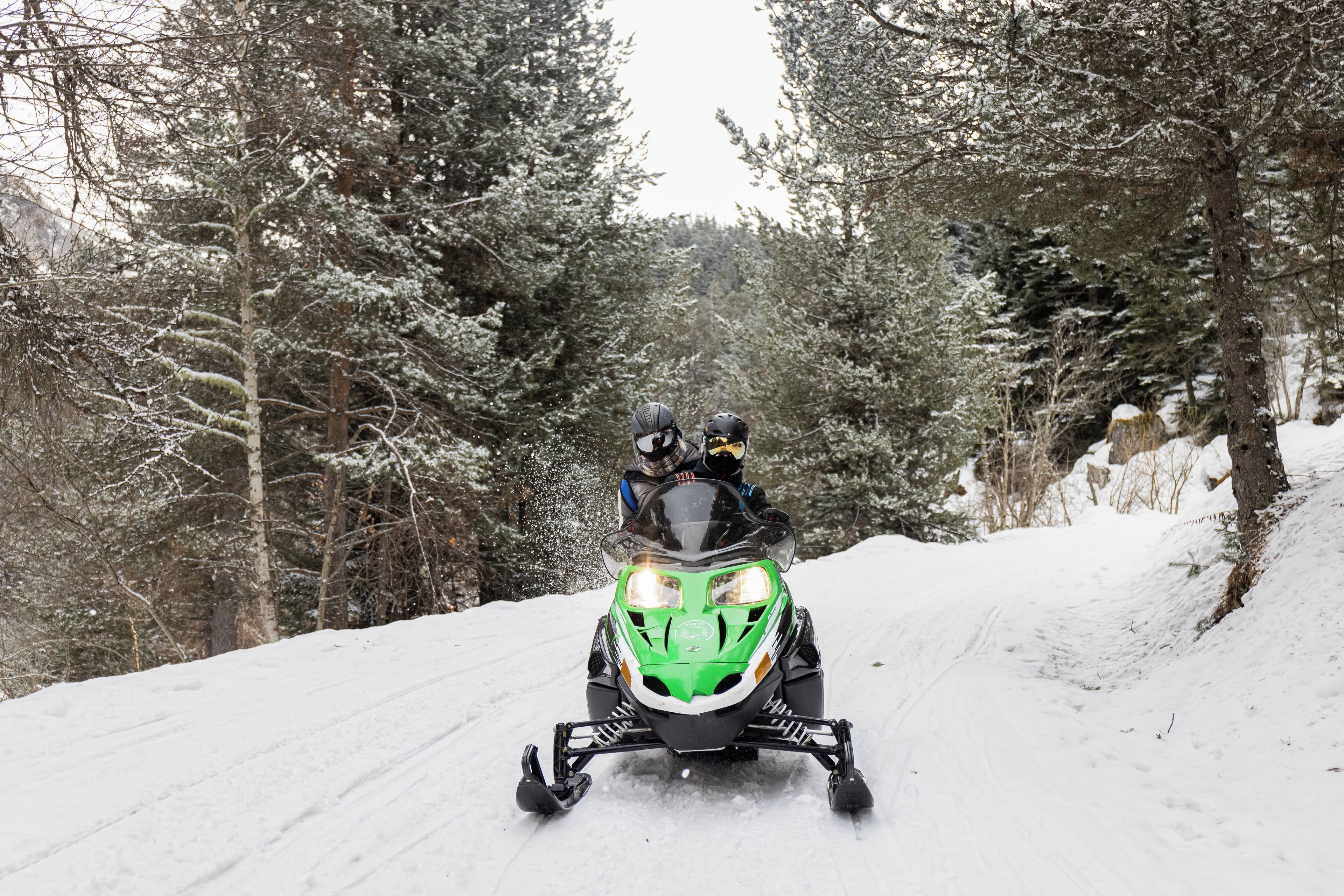Un vehículo para nieve circulando por un sendero cubierto de nieve, rodeado de árboles.