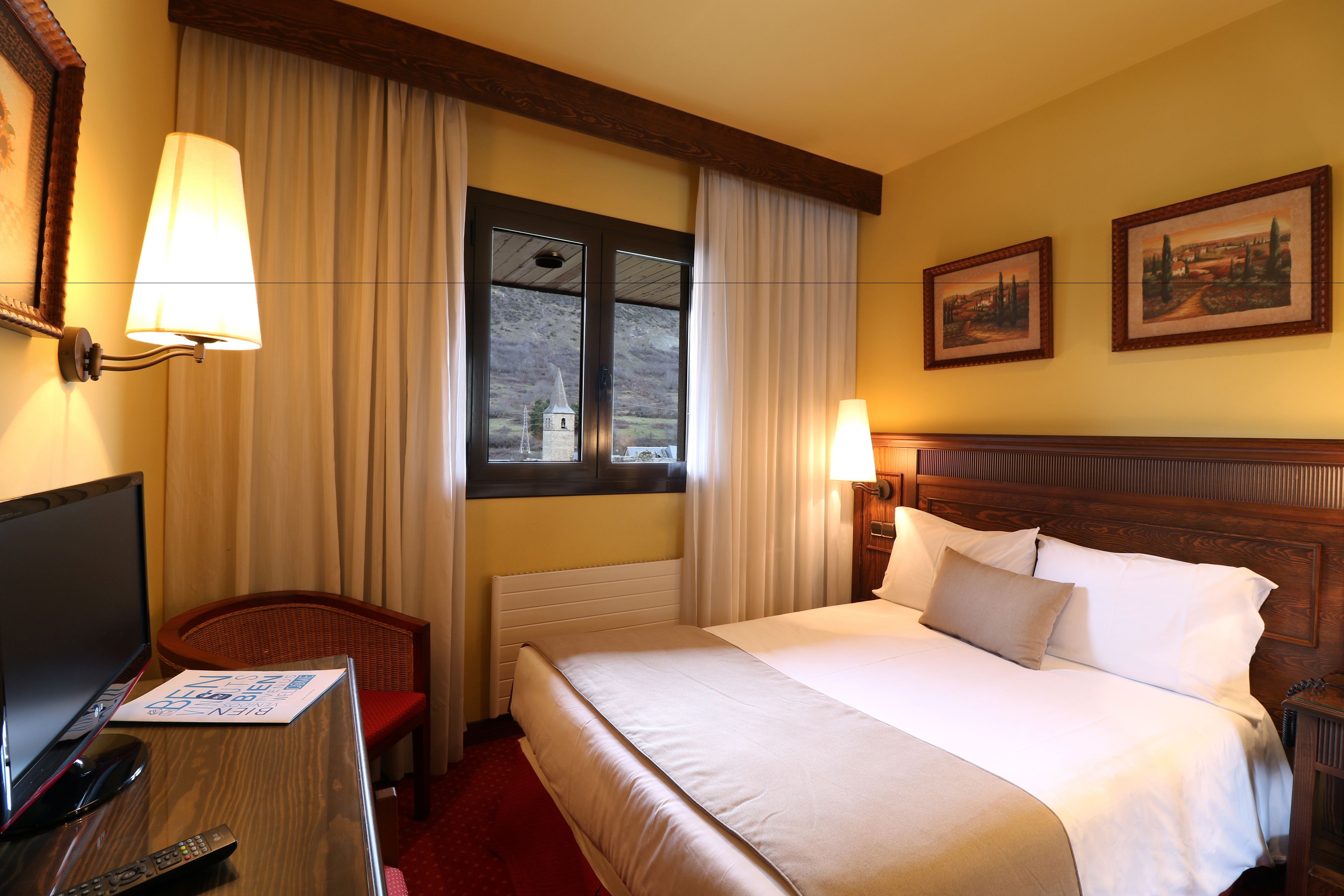 A hotel room with a large bed, a television, a desk with a remote control, and a window with curtains.