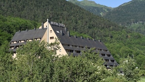 A hotel with a distinctive pyramid-like roof, surrounded by lush greenery and mountains. -  RVHotels Tuca (Vielha e Mijaran)