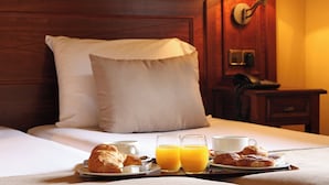 A neatly made bed with pillows, a bedside table with a lamp, and a tray with croissants, juice, and coffee. -  RVHotels Tuca (Vielha e Mijaran)