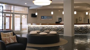 A lobby with a reception desk, a stone wall, and a seating area with ottomans. -  RVHotels Tuca (Vielha e Mijaran)
