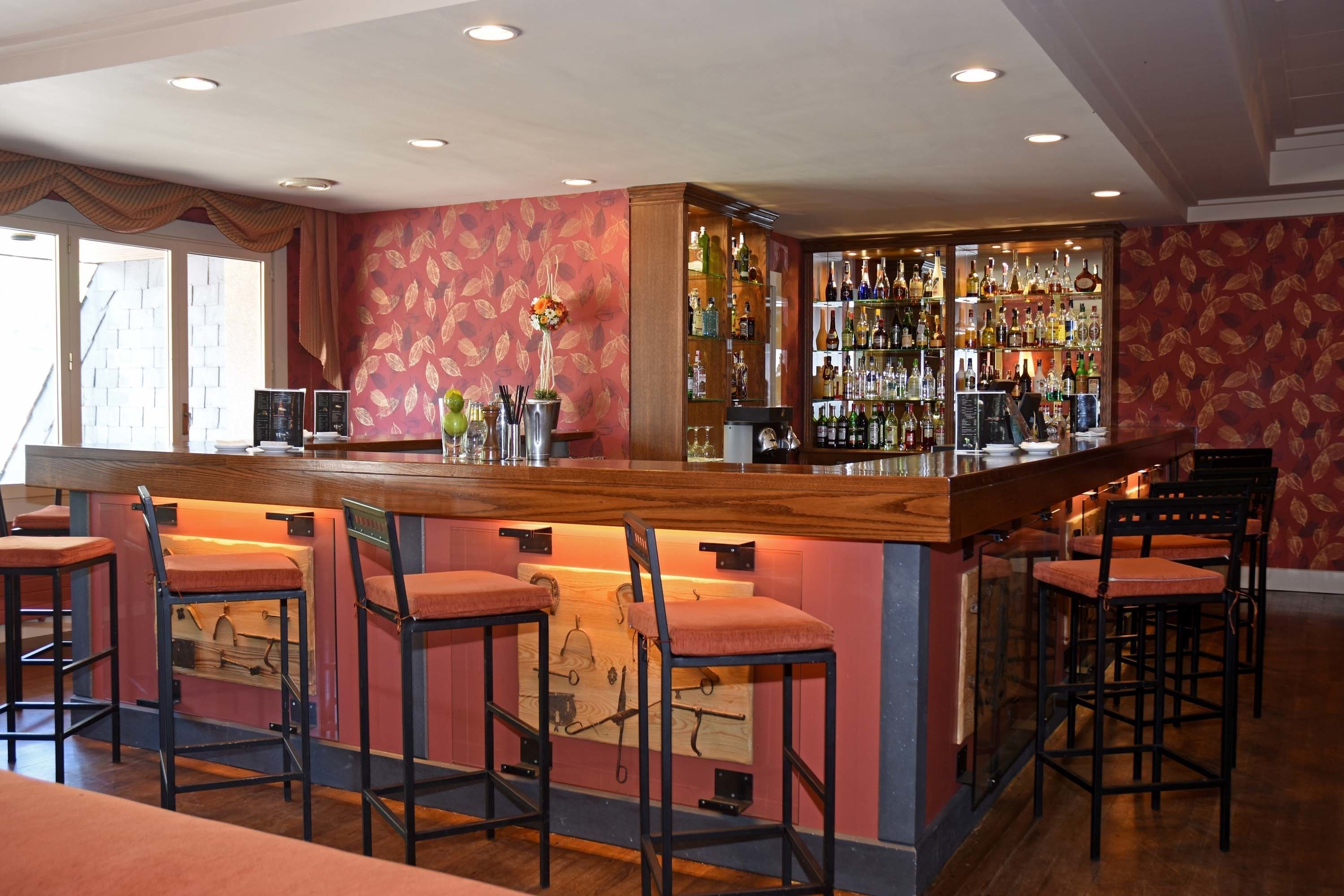 A bar area with a wooden counter, multiple stools, and a wall of liquor bottles.