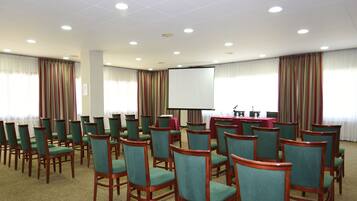Un salón de conferencias con filas de sillas de madera y una pantalla grande al frente.