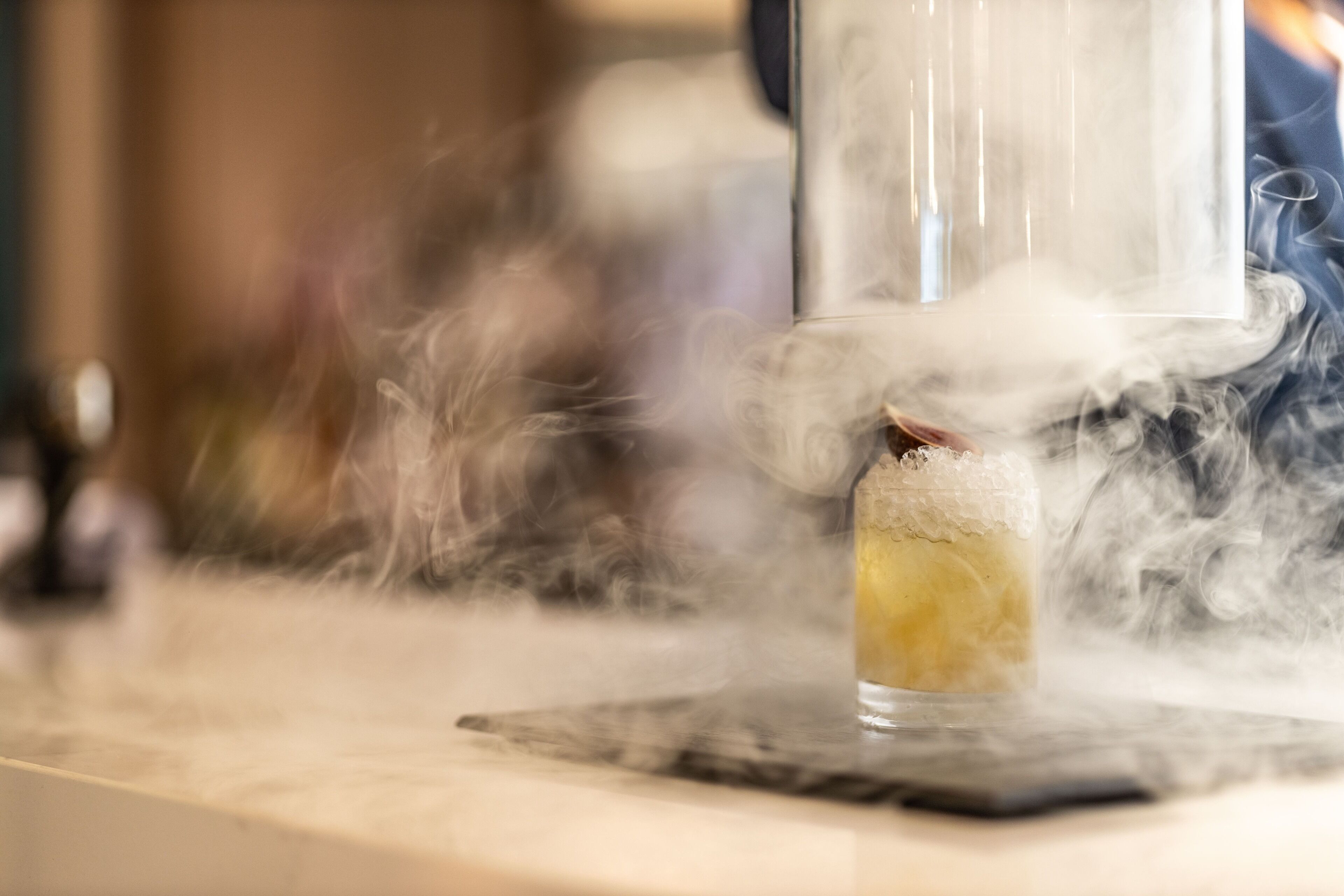 A glass with a yellowish liquid and a white substance, possibly ice, on a marble surface.