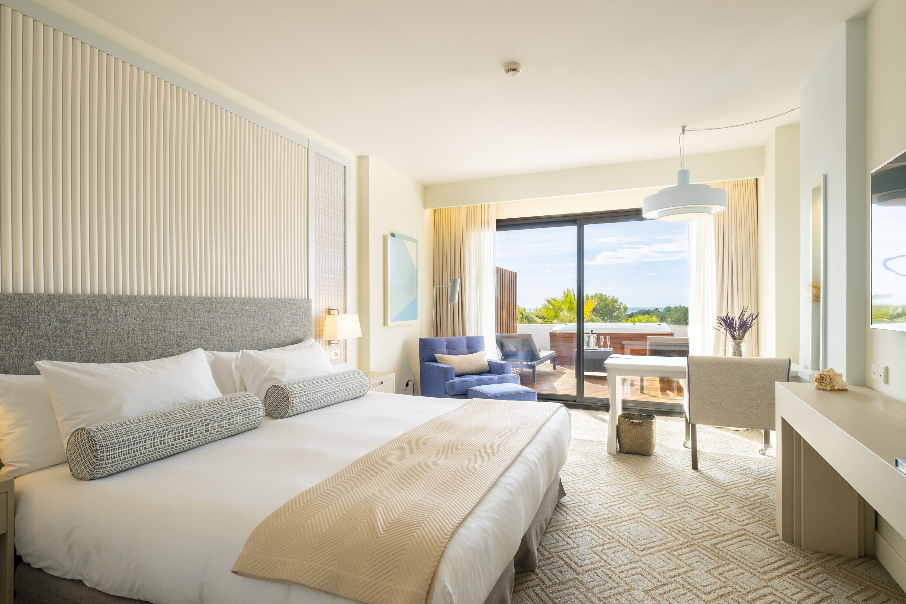A hotel room with a large bed, a desk, a chair, and a view of the outdoors.