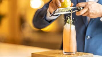 Eine Person reibt Zitronenschale über einen Drink in einem hohen Glas.