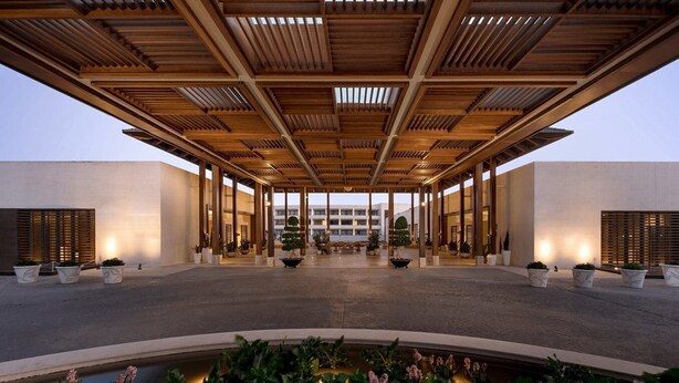 A spacious indoor area with a wooden ceiling structure, potted plants, and a central water feature.
