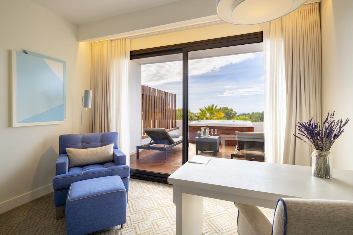 A modern hotel room with a blue sofa, a white table, and a view of the outdoor balcony.