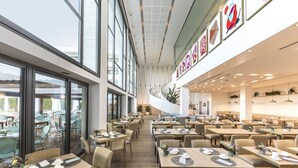 A modern dining area with multiple tables and chairs, large windows, and a spiral staircase.
