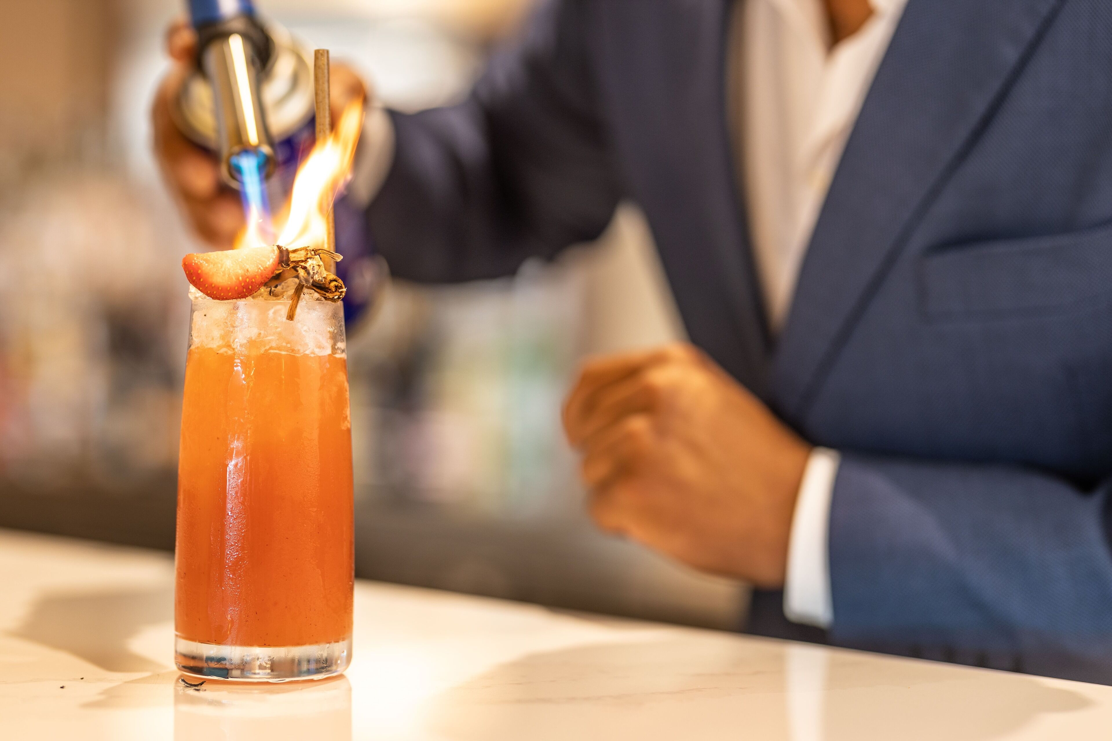 A cocktail with a flaming garnish on a bar counter.
