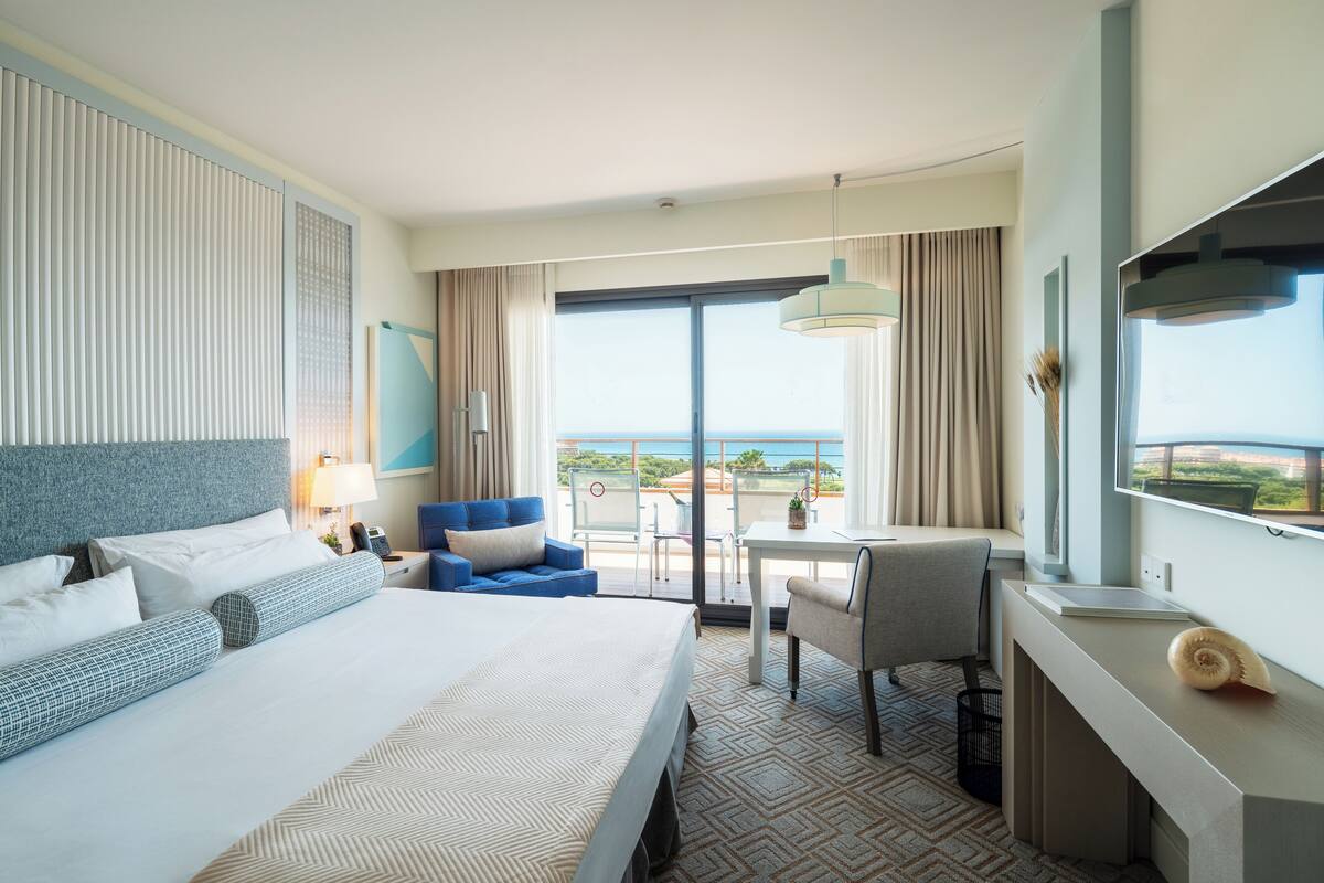 A hotel room with a large bed, a desk, a chair, and a view of the ocean.