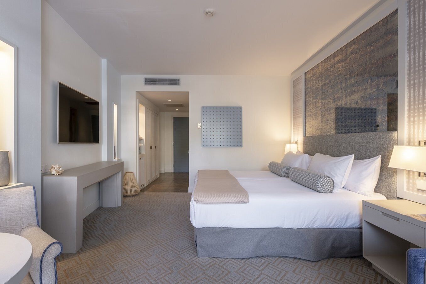 A modern hotel room with a large bed, bedside tables, a desk, and a television.