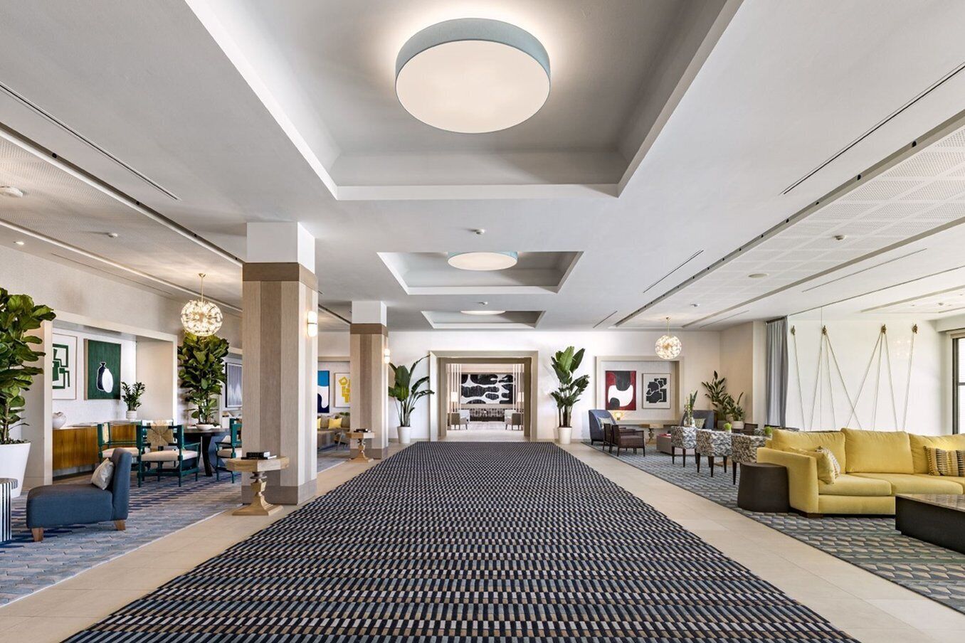 A spacious lobby with a central black and white patterned rug, a yellow sofa, and a reception desk with chairs.
