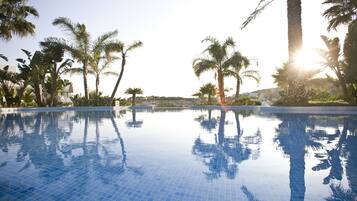 Une piscine d’un bleu éclatant, entourée de palmiers, avec un soleil radieux en arrière-plan.