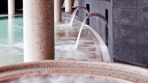 A modern indoor pool area with a central water feature, surrounded by columns and a curved ceiling.