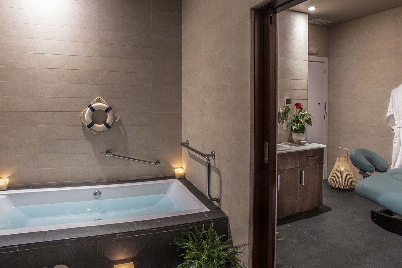 Un bany modern amb una banyera gran, barres de sujeció, un lavabo i una cadira de massatge.
