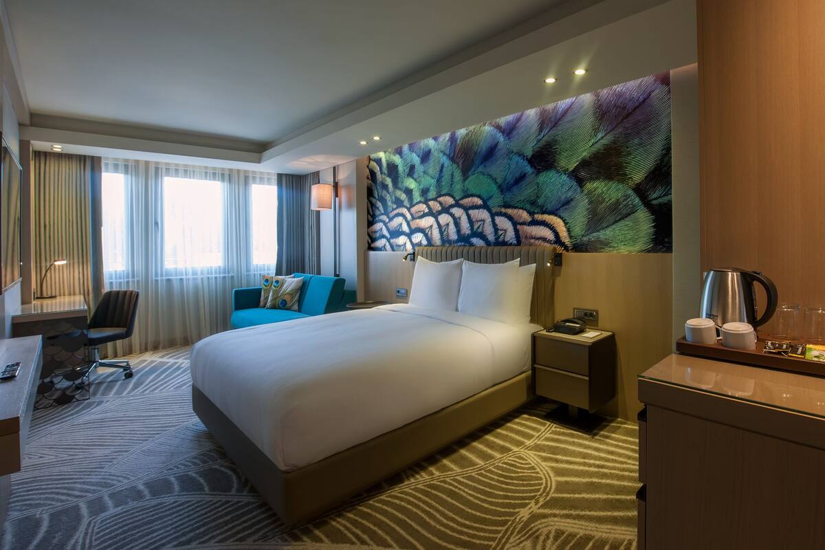 A hotel room with a large bed, a desk, a chair, a nightstand, and a coffee station.