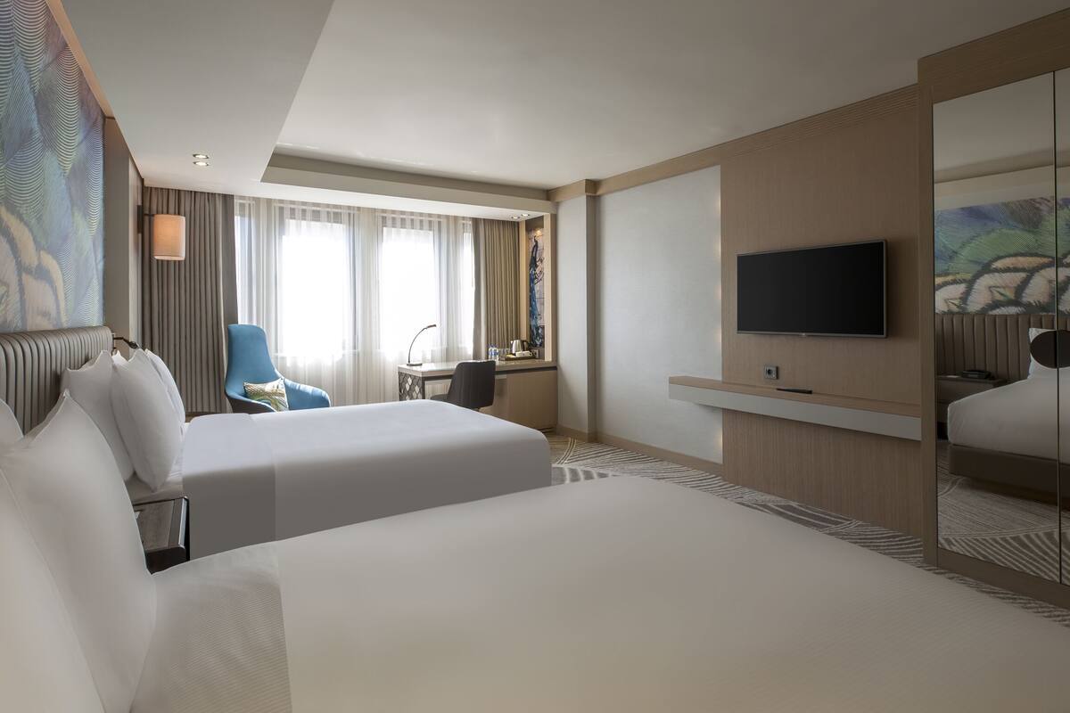 A hotel room with two beds, a desk, a chair, a television, and a large mirror.