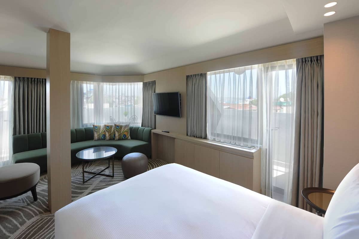 A hotel room with a bed, a sofa, a small round table, a chair, and a TV mounted on the wall.