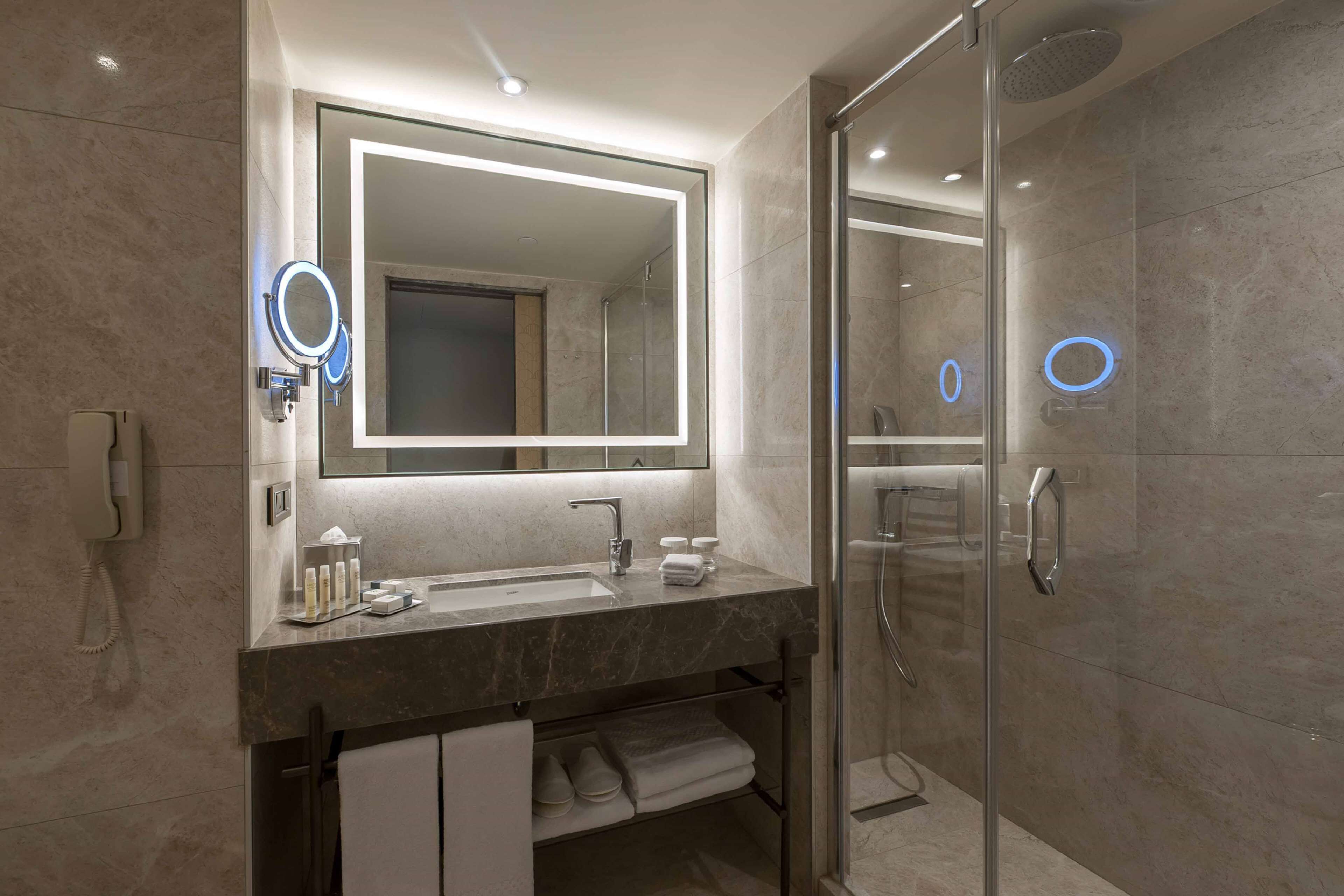 Un baño moderno con un espejo grande, un lavabo y una ducha con mampara de vidrio.
