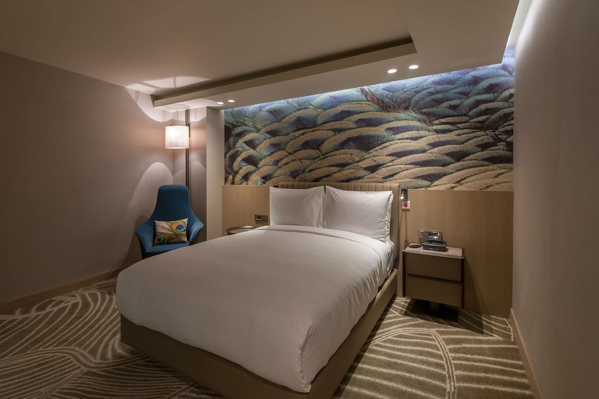A hotel room with a large bed, a chair, a nightstand, and a wall mural.