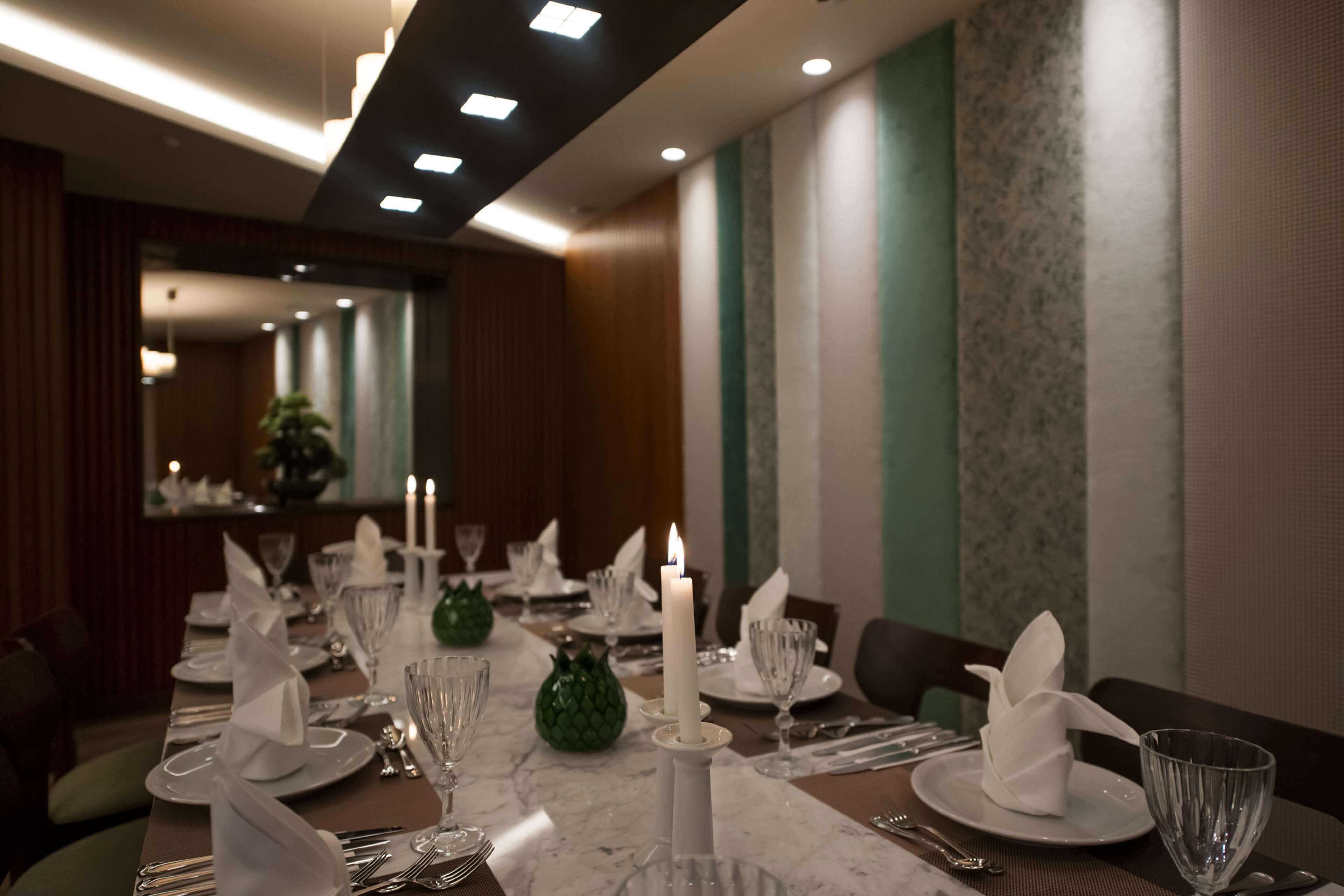 A dining area with a long table set for a meal, featuring white plates, silverware, and a lit candle centerpiece.