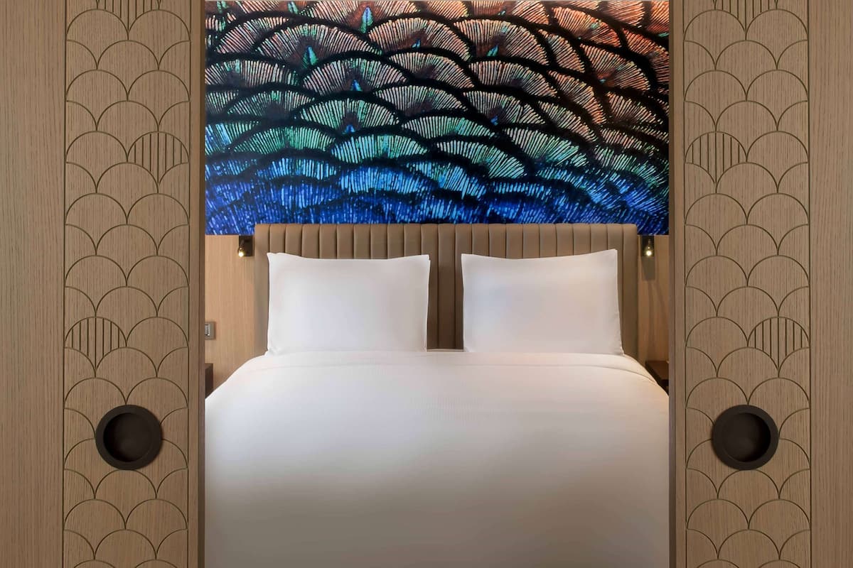 A modern hotel room with a large bed, a headboard with a decorative light panel, and a wooden panel design on the walls.