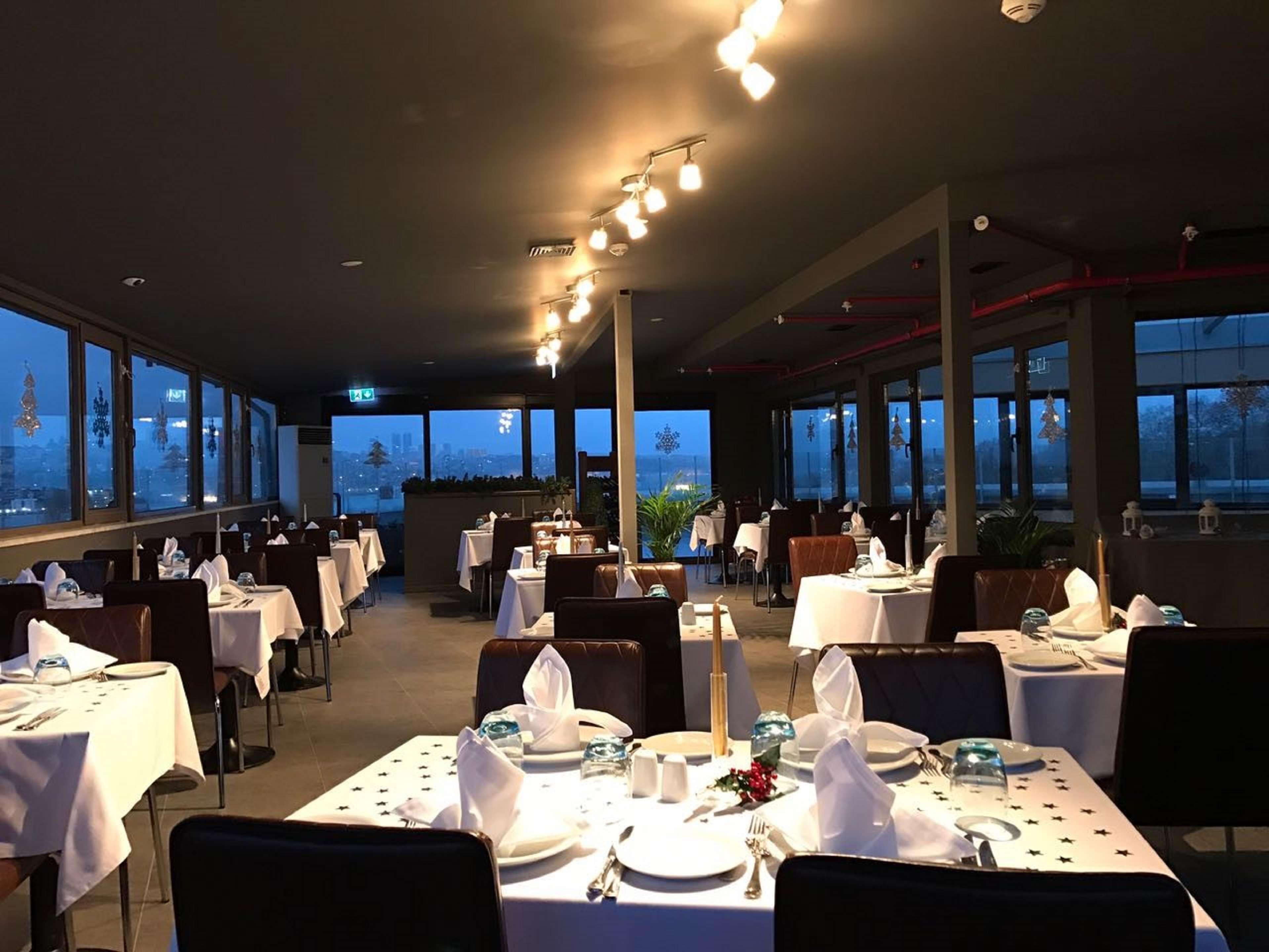 A restaurant with tables set for dining, large windows, and a city view.