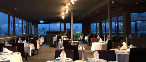 A restaurant with tables set for dining, large windows, and a city view.
