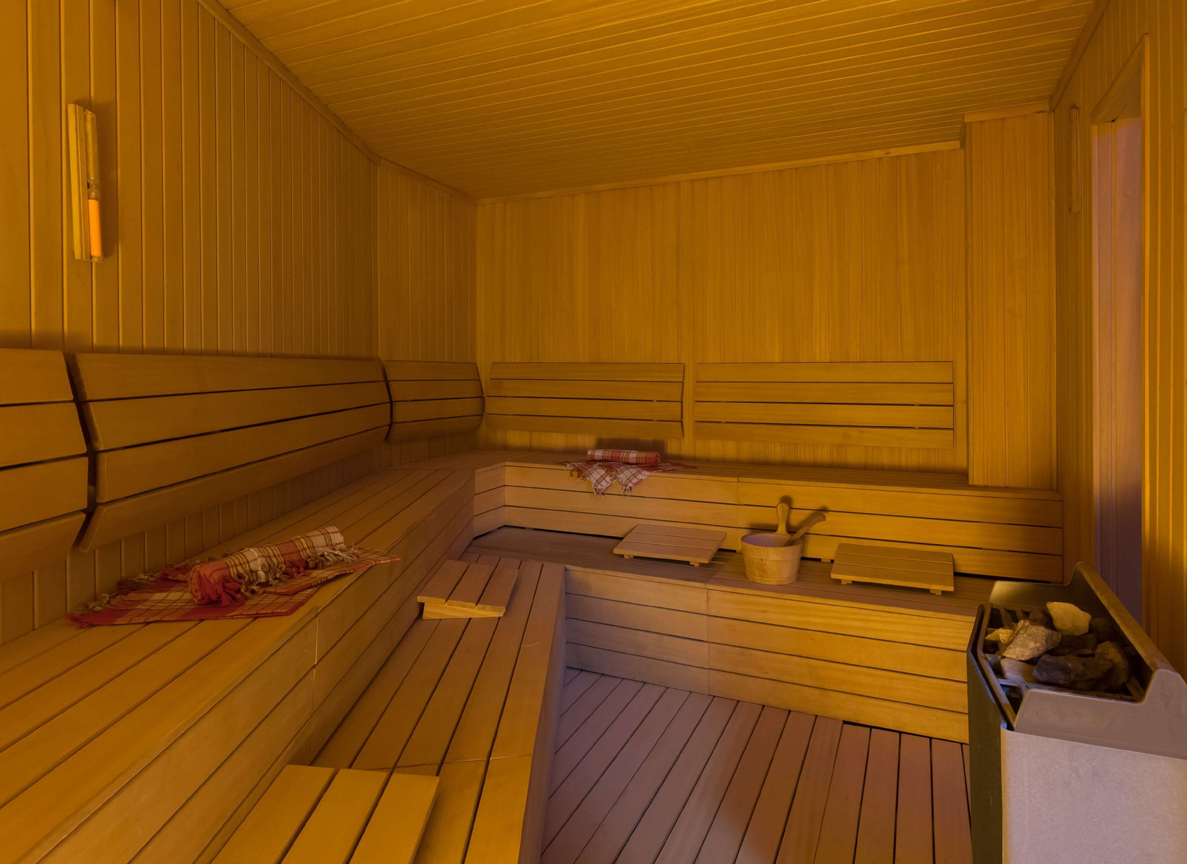 A sauna with wooden benches, a bench with a towel, and a bucket with rocks.