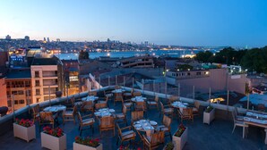 A rooftop terrace with tables and chairs, overlooking a cityscape and water body. - DoubleTree by Hilton Hotel Istanbul - Sirkeci (Istanbul)