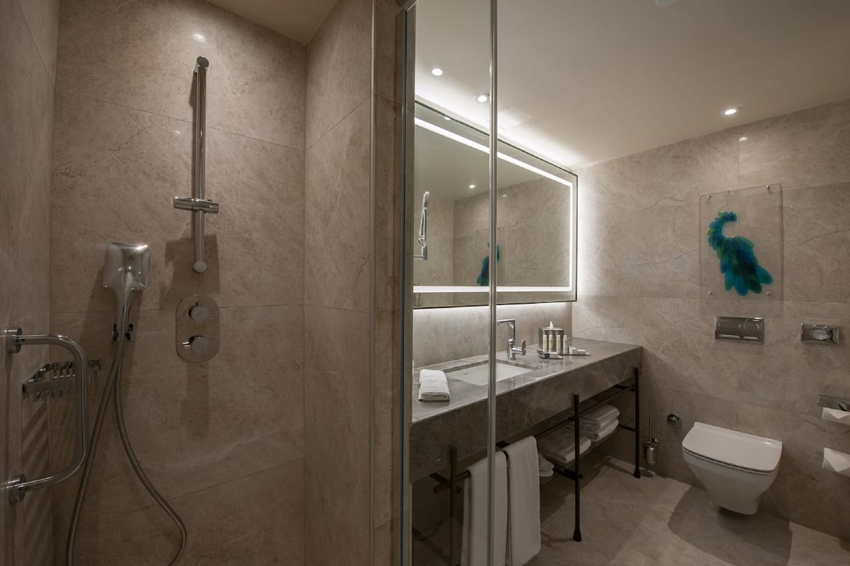 A modern bathroom with a glass shower enclosure, a large mirror, a toilet, and a sink with a towel rack.