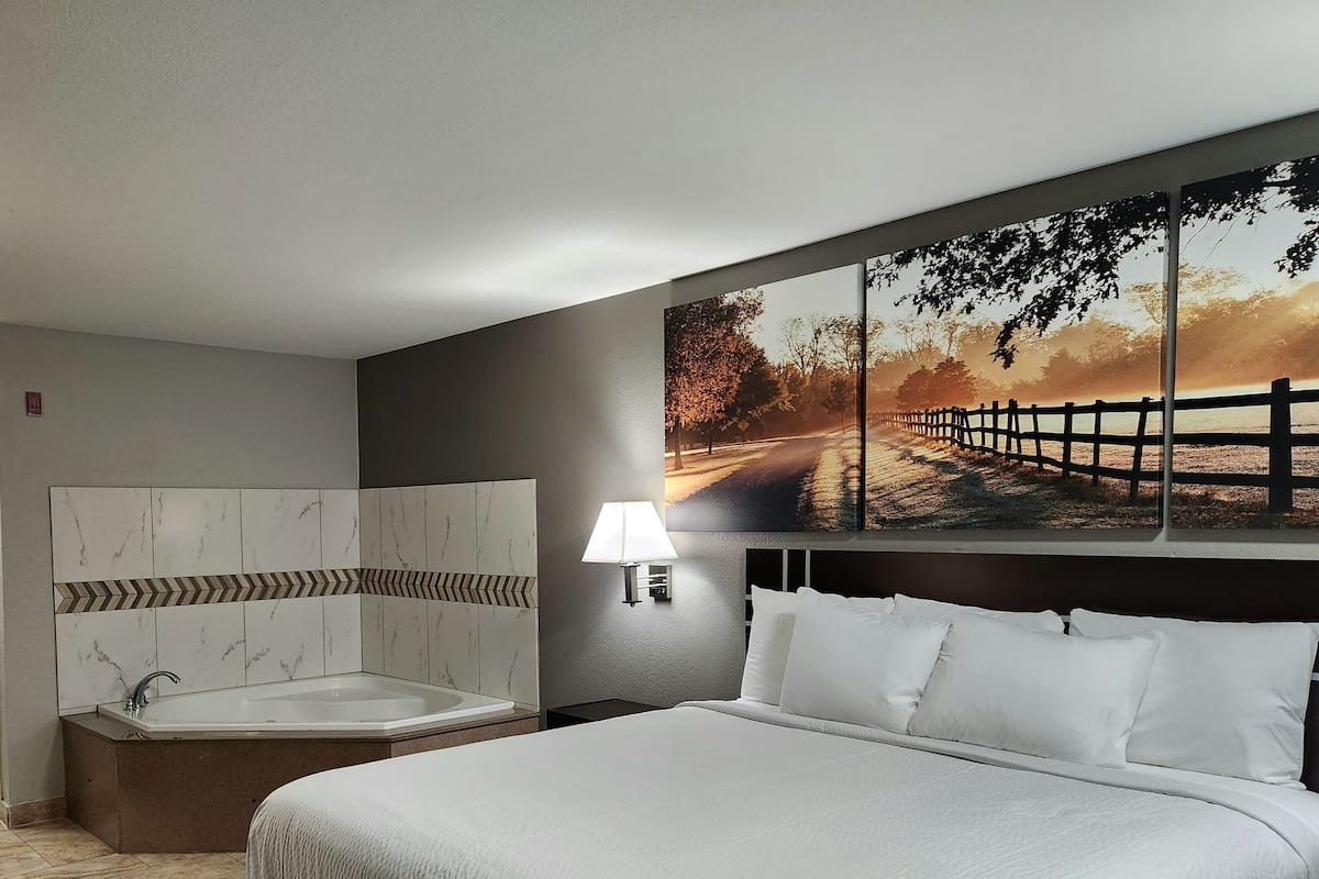 A hotel room with a large bed, a bathtub, and a wall-mounted shower.