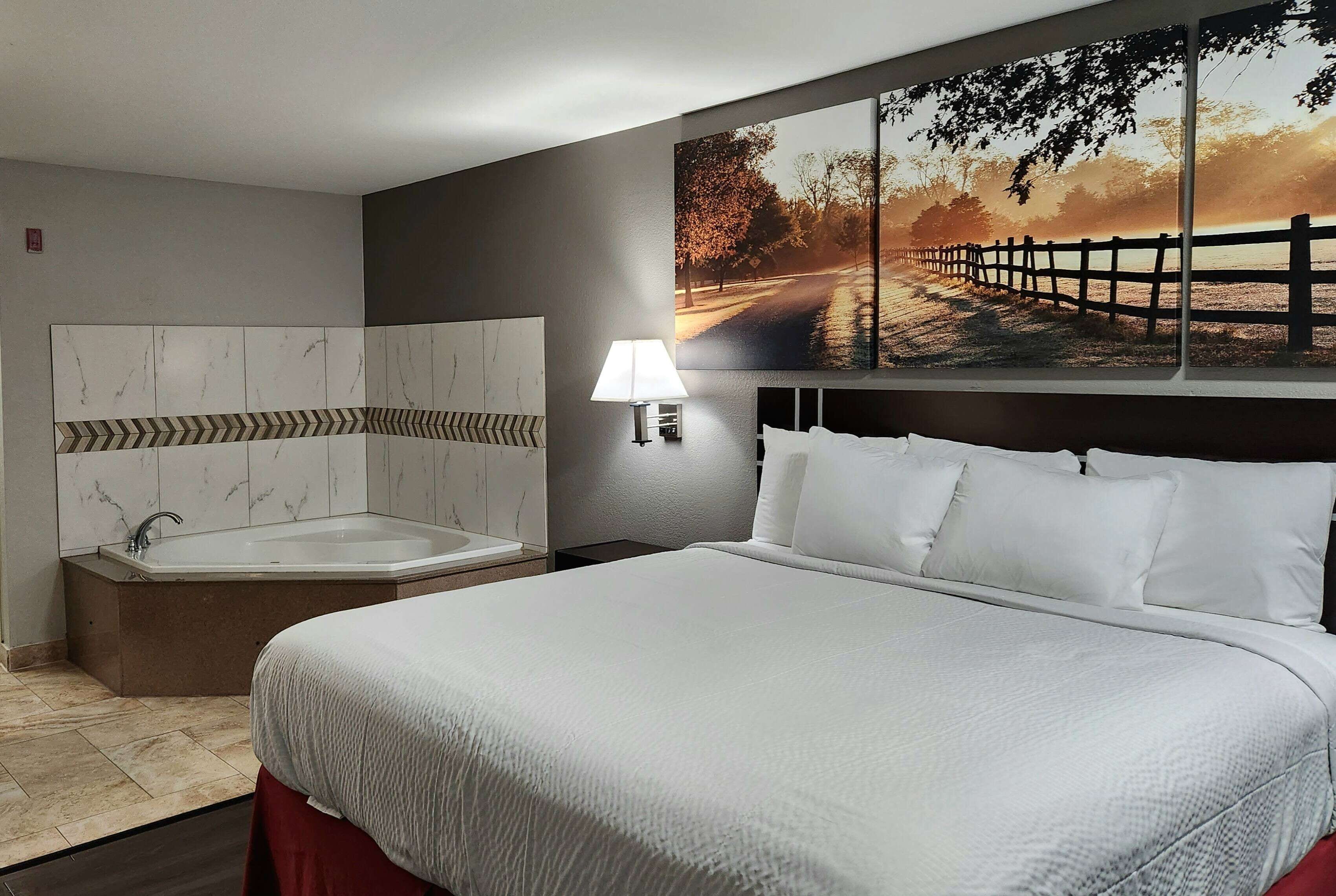 Una habitación de hotel con una cama grande, un baño con bañera y un cuadro de un atardecer sobre un puente.
