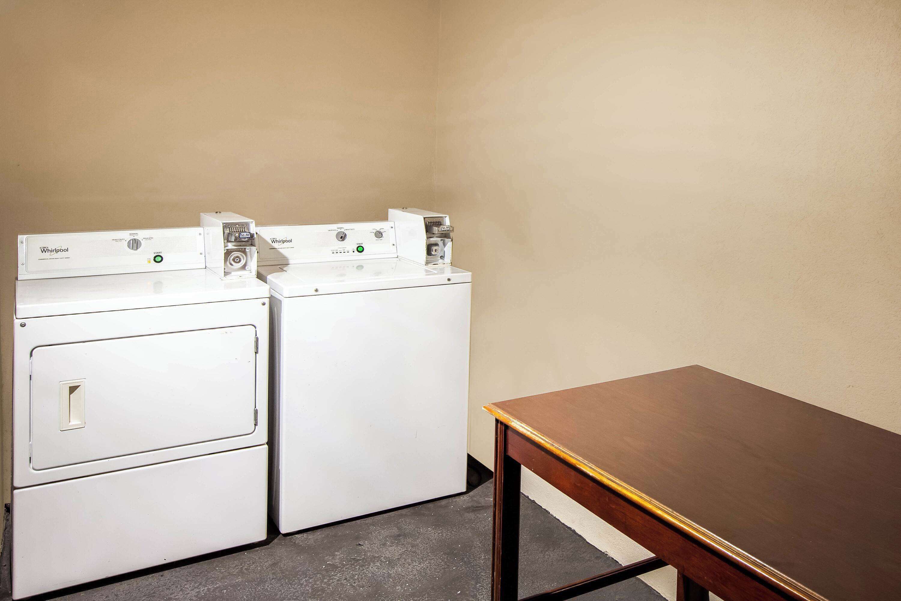 A laundry room with two stacked washers and dryers, a wooden table, and a plain wall.