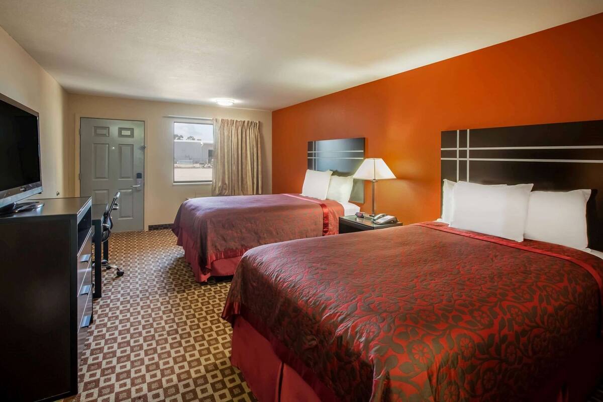A hotel room with two beds, a TV, a desk, and a window with curtains.