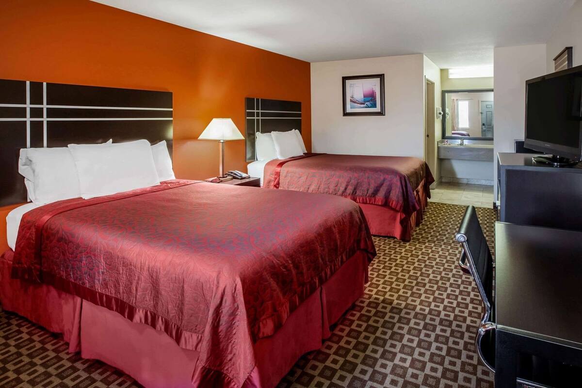 A hotel room with two beds, a TV, and a desk.