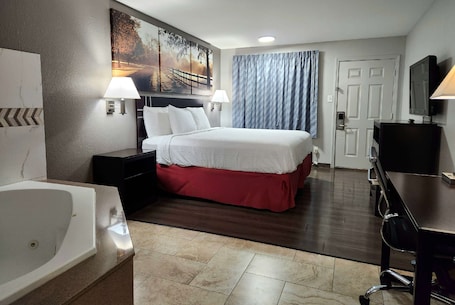 A hotel room with a large bed, a desk, a chair, a TV, a desk lamp, a wall-mounted TV, a painting, a window with curtains, and a bathroom with a bathtub and sink.