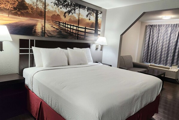 A hotel room with a large bed, a headboard with storage, a desk, a chair, a wall-mounted lamp, and a window with curtains. - Days Inn by Wyndham Sulphur LA (Sulphur)