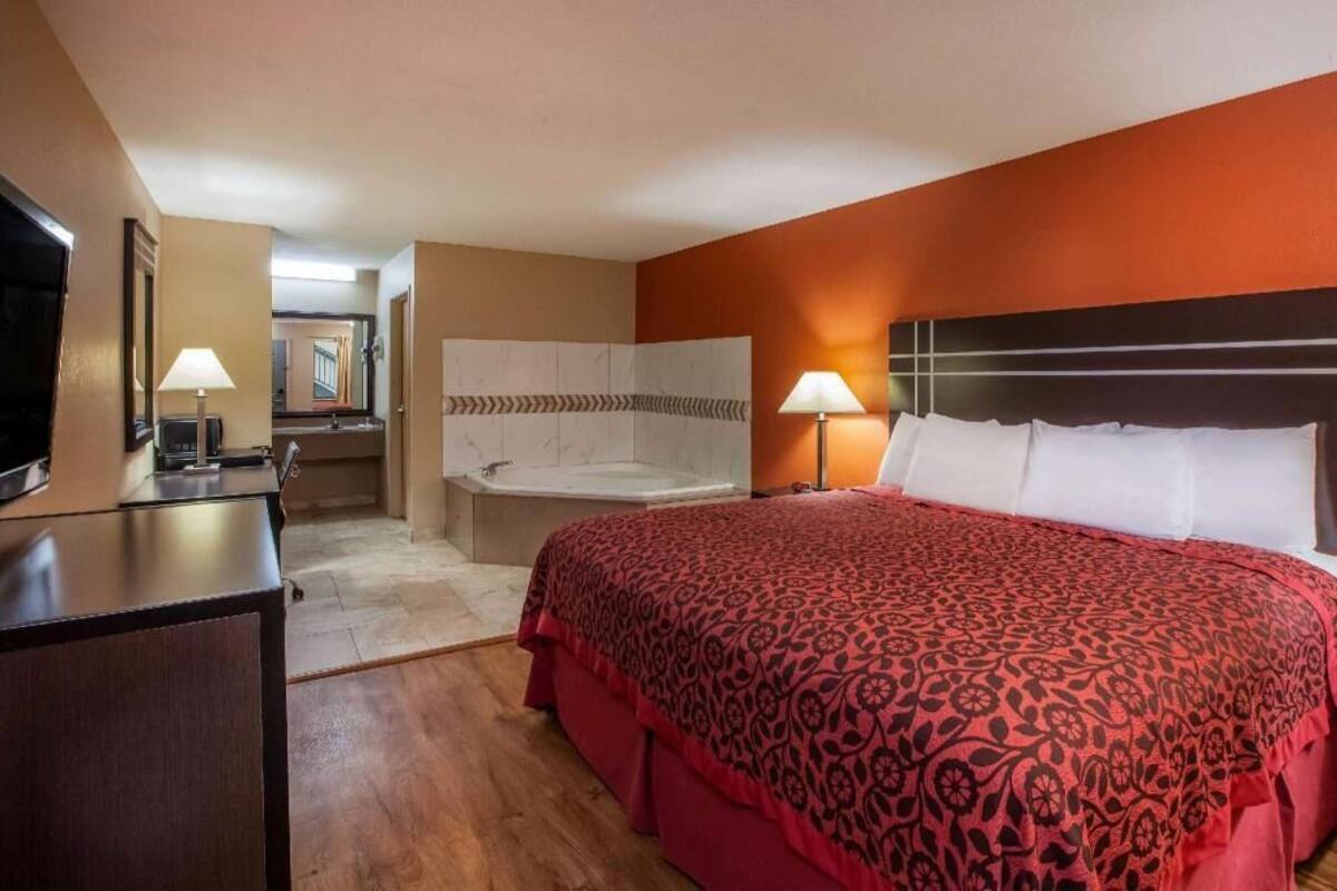A hotel room with a large bed, a desk with a lamp, a bathroom with a bathtub, and a TV.