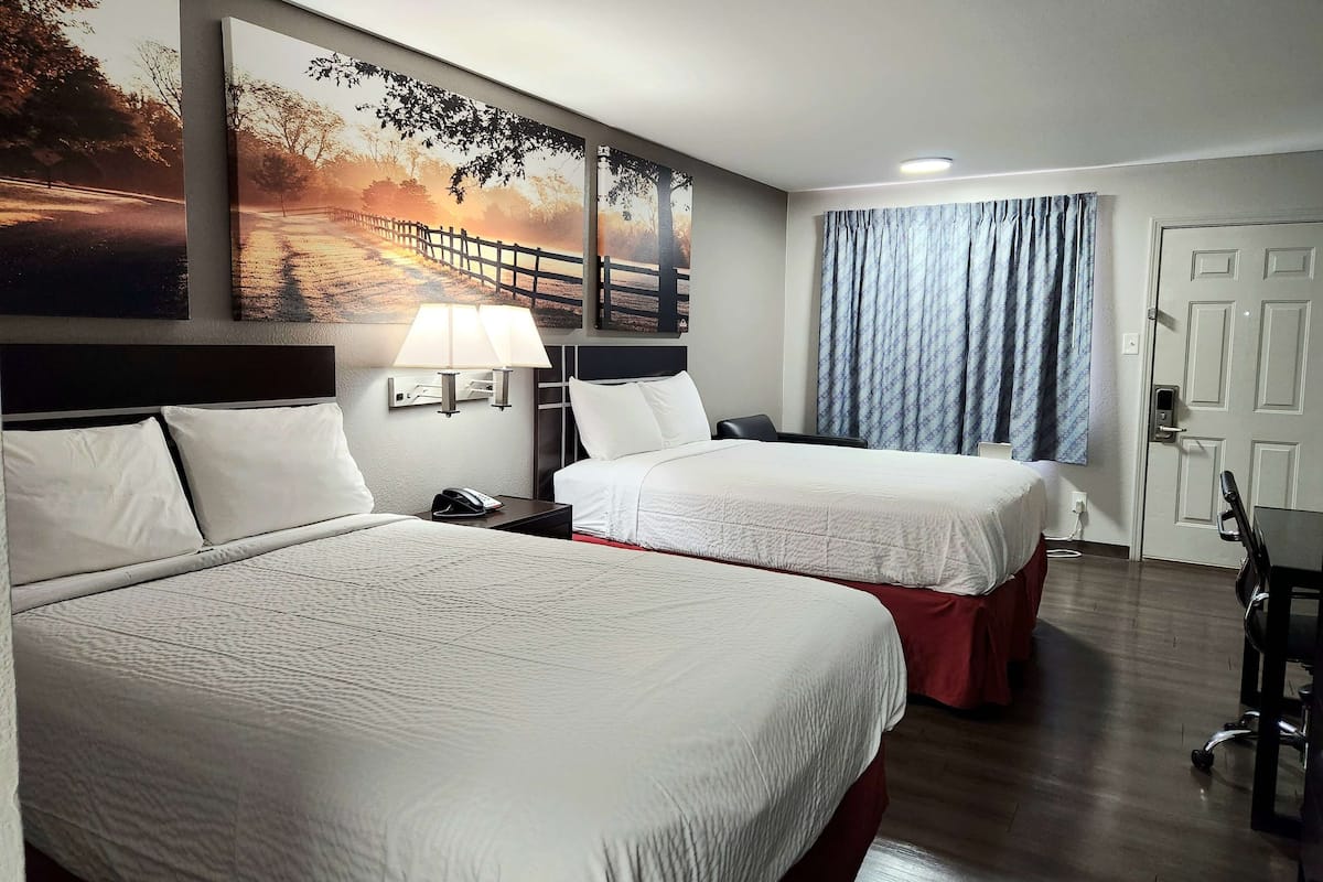 A hotel room with two beds, a desk, a chair, a lamp, and a window with curtains.