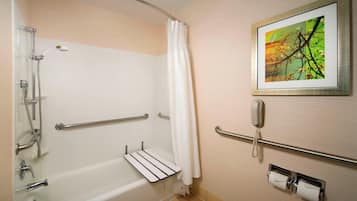 A bathroom with a bathtub, a shower, a handrail, a telephone, and a framed picture on the wall.
