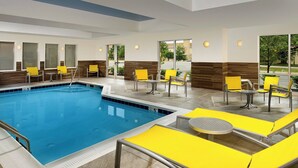 A swimming pool area with yellow lounge chairs and tables, surrounded by windows with views of greenery. - Fairfield Inn & Suites Germantown Gaithersburg (Germantown)