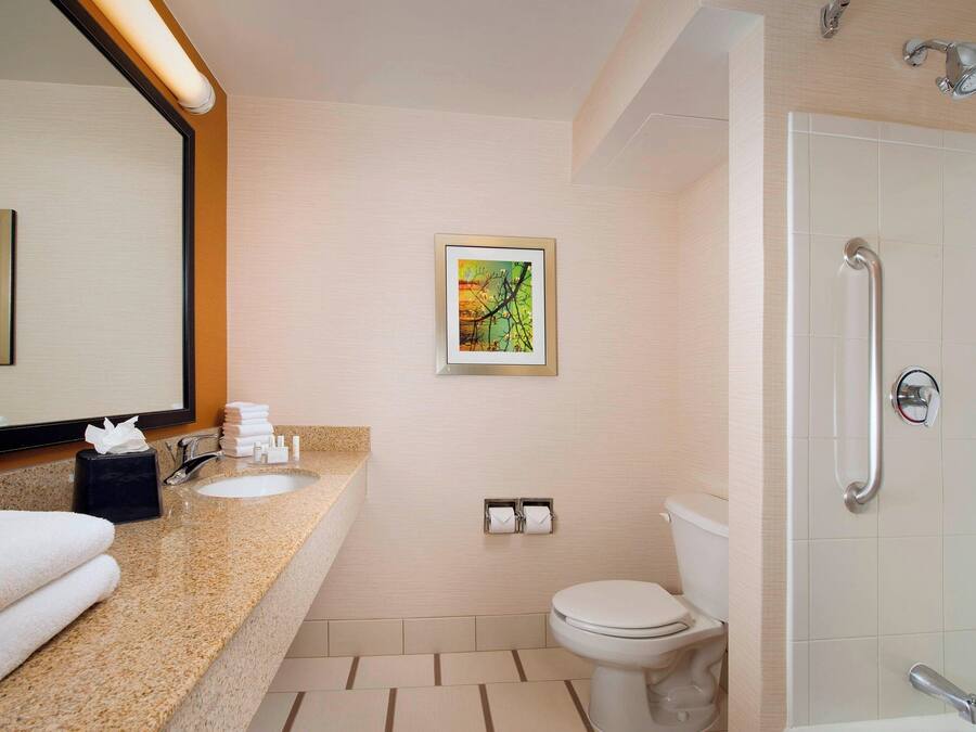 Un baño moderno con encimera de granito, inodoro, ducha con barra de apoyo y cuadros en la pared.