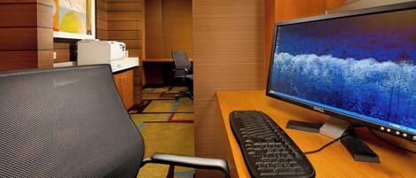 A hotel room with a wooden desk, a computer setup, and a chair.