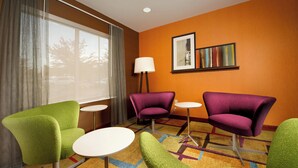 A hotel room with a large window, a lamp, and a colorful carpet. There are two green chairs and two purple chairs. - Fairfield Inn & Suites Germantown Gaithersburg (Germantown)