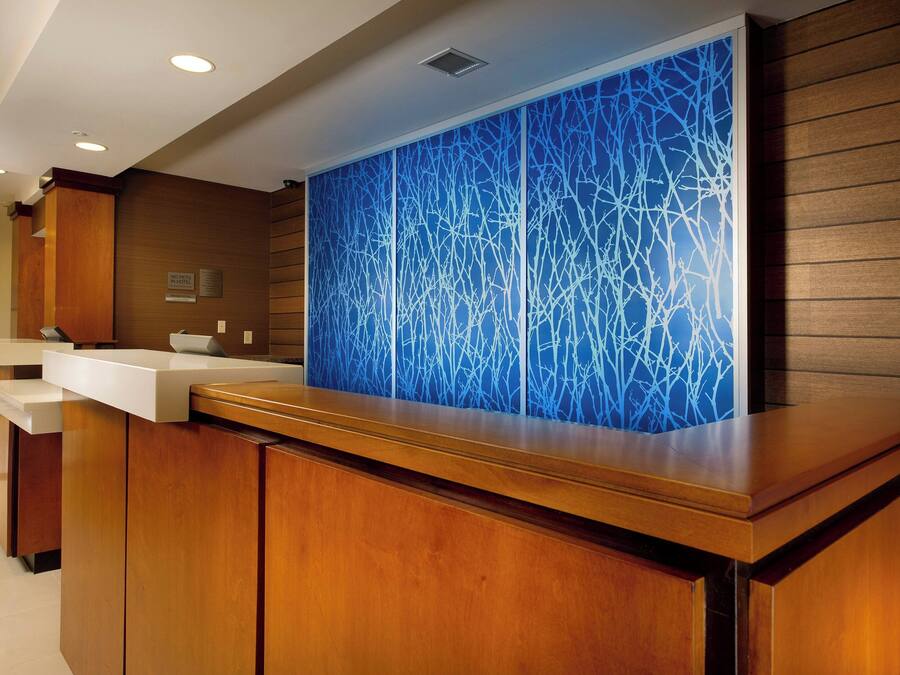 Una zona de recepción con mostrador de madera, pared decorada con un diseño abstracto azul y un letrero que indica área para no fumadores.