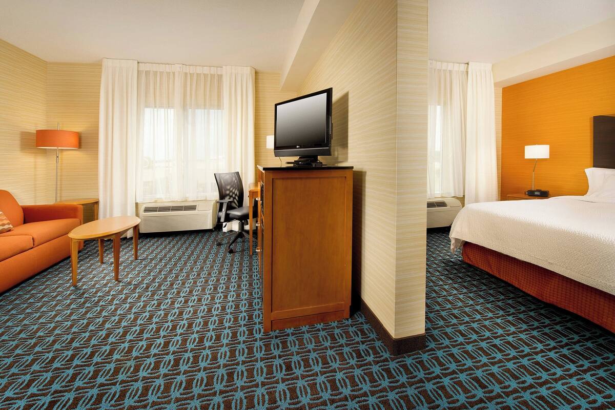A hotel room with a bed, a desk with a television, a chair, and a sofa.